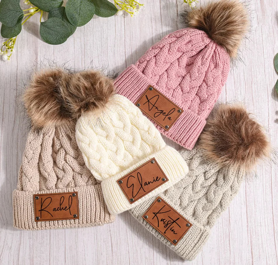 Drei gestrickte Babymützen mit Bommel und Namenspatches mit den Namen Rachel, Elanie und Kristin