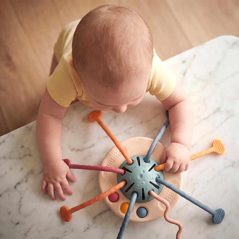 Baby zieht auf dem Bauch an den Bändern des Spielzeugs