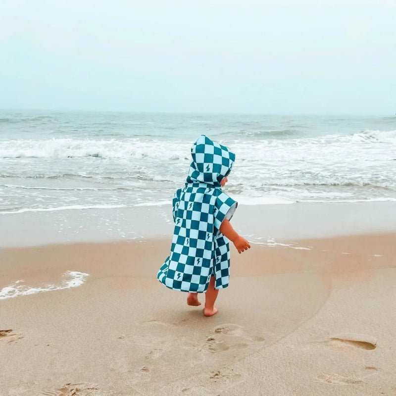 Kind läuft in einem blauen Badeponcho am Meer entlang