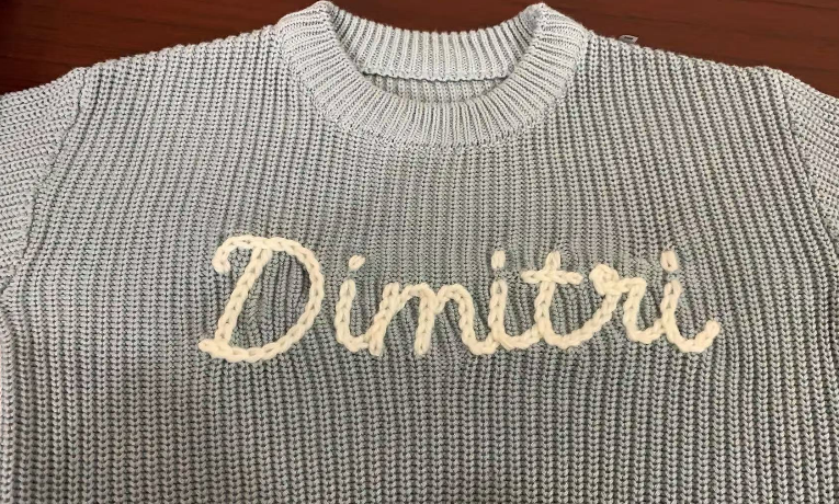 Nahaufnahme des handbestickten Namens Dimitri auf einem grauen Pullover
