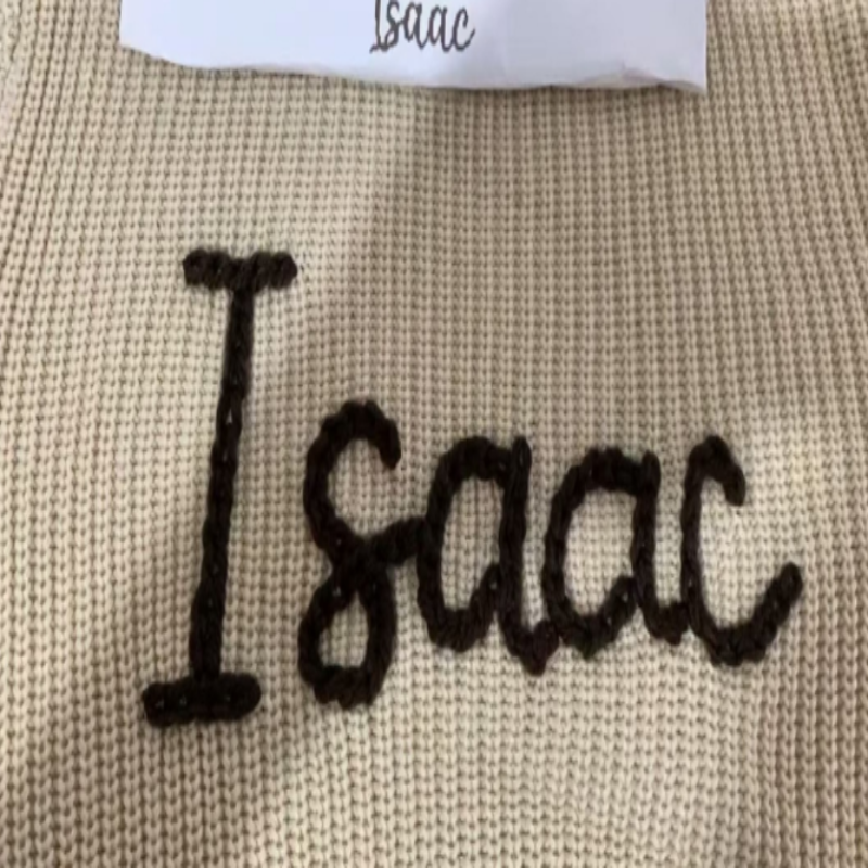 Nahaufnahme des handbestickten Namens Isaac in dunklem Garn