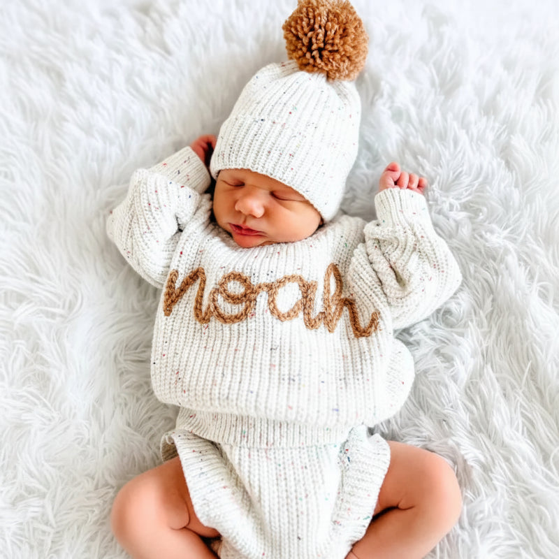 Neugeborenes in einem gestrickten Pullover mit dem gestickten Namen Noah